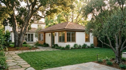 A detached backyard guest house behind a Brentwood single-family home, surrounded by lawn and mature trees