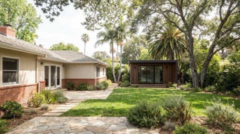 A backyard accessory dwelling unit tucked behind a traditional single-family home under mature trees.