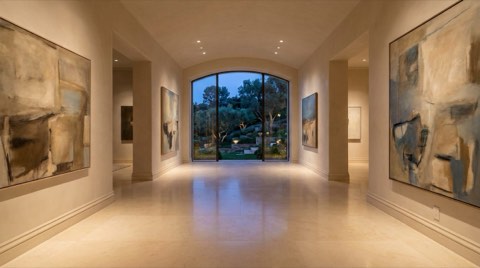 An elegant private art gallery hallway inside a Bel Air estate, with abstract art and a hillside view at dusk