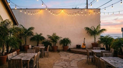 An intimate outdoor courtyard with string lights and potted palms at dusk in a quiet beach town
