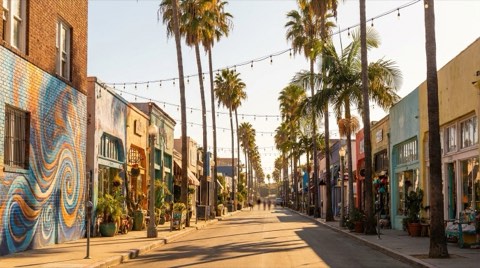 A colorful mural-lined Venice boutique street with string lights at golden hour