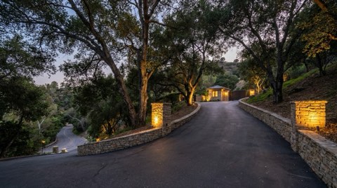 A long private driveway winding down a Bel Air hillside toward a quiet canyon road at dusk