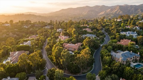 A golden-hour view across the rolling hillside estates of Bel Air, rooftops emerging from mature greenery