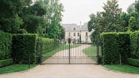A gated Bel Air estate with a closed wrought iron gate and long private driveway under soft overcast light