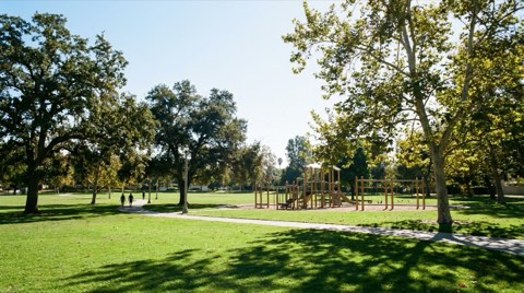 A sunny neighborhood park near Beverlywood with a green lawn, walking path, and playground in the distance