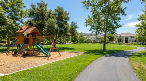 A green neighborhood park with a play structure and shade trees on a sunny day
