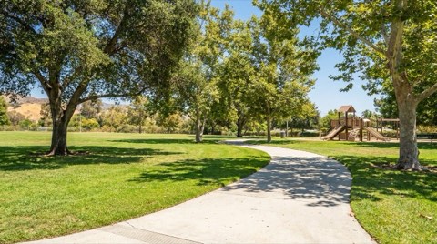 A sunny neighborhood park path in Studio City with green lawn and a playground in the distance