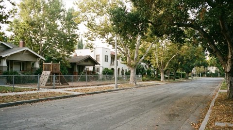 A quiet residential street near a small neighborhood schoolyard in the morning light.