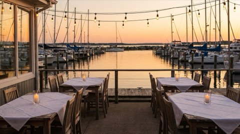 A quiet restaurant patio at sunset with candlelit tables overlooking a calm marina