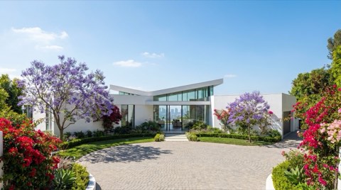 A pristine white modern hillside estate with blooming jacaranda trees and a circular driveway under clear blue spring morning light