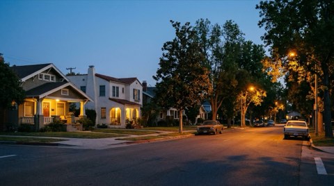 A quiet residential street with traditional homes and glowing porch lights at dusk