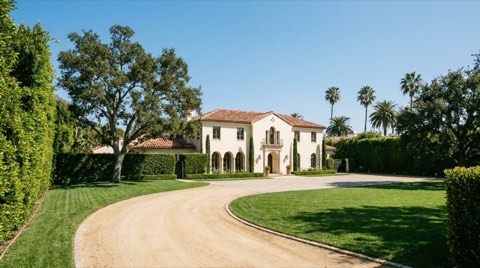 A stately single-family estate home with a manicured lawn and long driveway in an affluent Los Angeles neighborhood