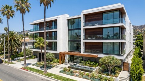 A modern four-story apartment building with balconies and a landscaped entrance