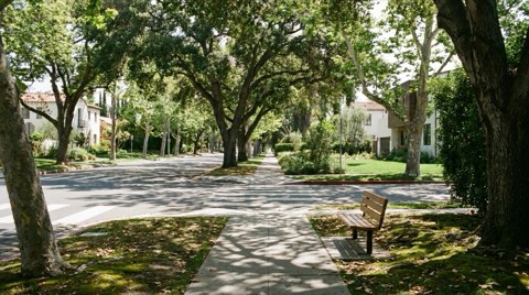 A tree-shaded sidewalk with a crosswalk along a quiet upscale residential street