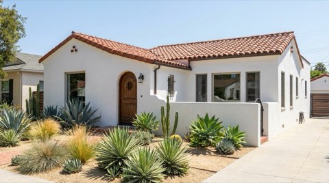 A Spanish Colonial Revival home exterior with white stucco walls and a terracotta tile roof under clear midday sun