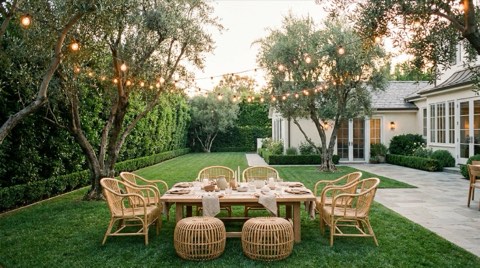 An elegant backyard garden party setup with string lights and empty rattan chairs at dusk