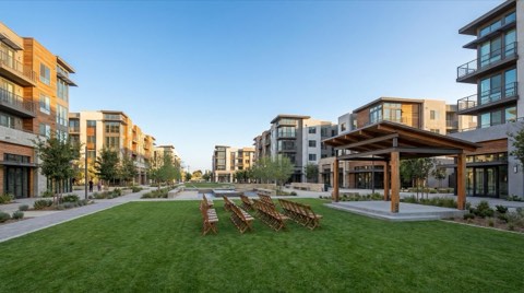 An open community lawn set up for a gathering with rows of empty folding chairs facing a small stage, under bright afternoon light.