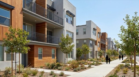 A street view of a row of modern condo and townhome buildings with varied but complementary contemporary facades under bright daytime light.