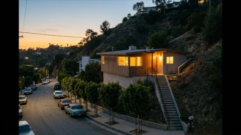 A small, cozy mid-century home tucked into a narrow winding Hollywood Hills canyon street, softly lit from within at dusk