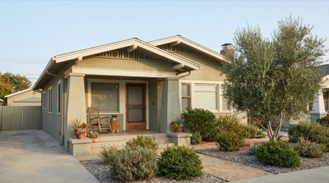 A modest 1930s bungalow home with a welcoming front porch in soft warm morning light