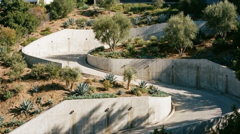 A steep hillside driveway supported by engineered concrete retaining walls with terraced drought-tolerant landscaping