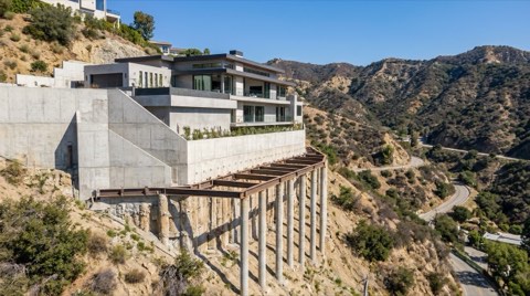 A hillside home built into a steep slope with visible retaining walls and canyon terrain behind it
