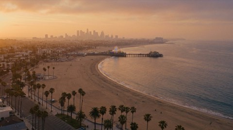 An elevated view of the Santa Monica pier, beach, and coastline with the downtown skyline in the distance