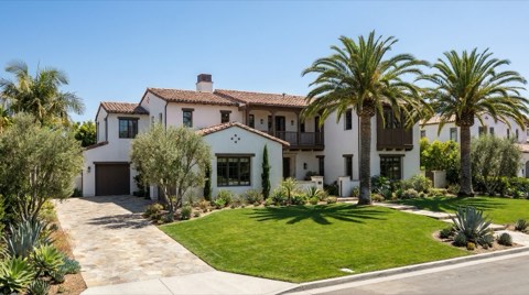 A grand upscale single-family home exterior with a manicured front lawn under clear daytime sky