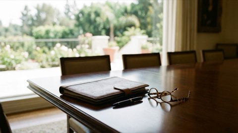 A polished dining table with a closed leather portfolio and pen beside a soft-lit garden view