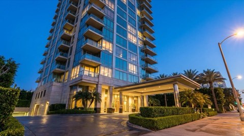 A Wilshire Corridor style high-rise condo tower in Westwood photographed from a low angle at dusk with warm lights glowing in the windows against a blue twilight sky