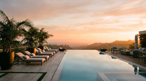 An infinity-edge pool terrace overlooking a hazy canyon at sunset with lounge chairs and potted palms