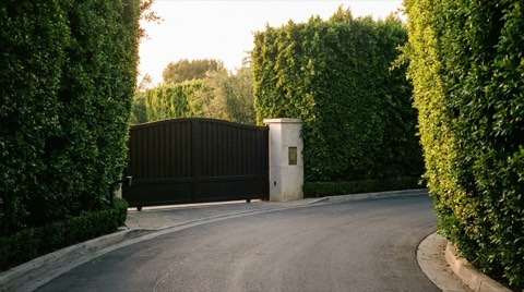 A discreet, generic gated estate entrance with tall hedges and a closed iron gate at golden hour