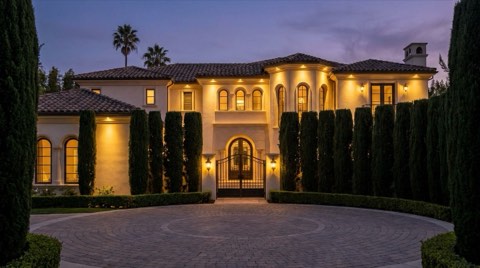 An elegant traditional estate home behind manicured hedges in Beverlywood at dusk
