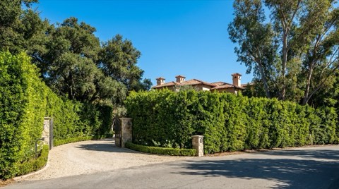 A private estate exterior with only glimpses of a rooftop visible above tall privacy hedges