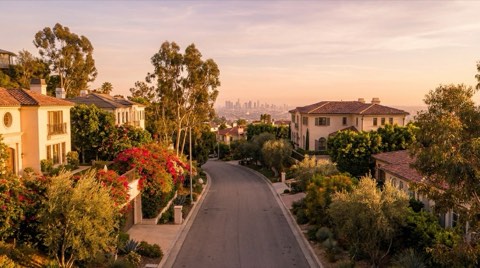 A peaceful Hollywood Hills street at golden hour with a view corridor opening between homes toward the distant city skyline