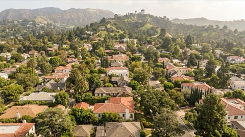 An aerial view of Los Feliz rooftops nestled among mature trees with Griffith Park's hills in the background