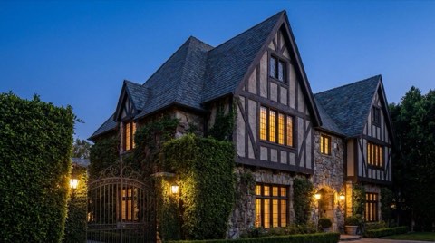 A grand Tudor revival estate in Los Feliz with ivy-covered stone walls and a wrought iron gate at dusk