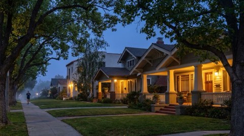A quiet tree-lined Los Feliz residential street with porch lights glowing at early evening blue hour
