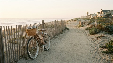 A bicycle parked along a beach path with dune fencing and soft morning ocean light