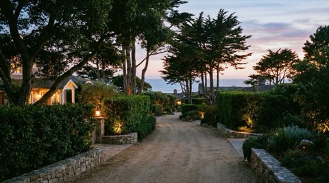 A quiet, private residential street with mature privacy hedges and warm porch lights at dusk