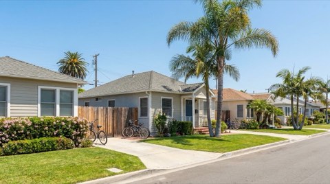 A calm, well-kept residential street with trimmed lawns under a clear blue sky