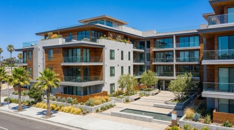 A modern multi-story condominium building exterior with clean architectural lines and landscaped courtyard, bright daylight.