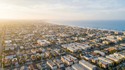 An elevated aerial view of Santa Monica rooftops and palm-lined streets with the Pacific Ocean coastline at sunrise