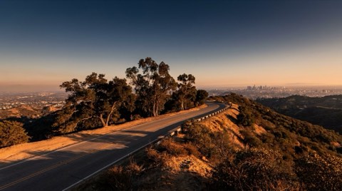 Mulholland Drive winding along a ridge in the Hollywood Hills at golden hour with sweeping views of the valley and the city basin