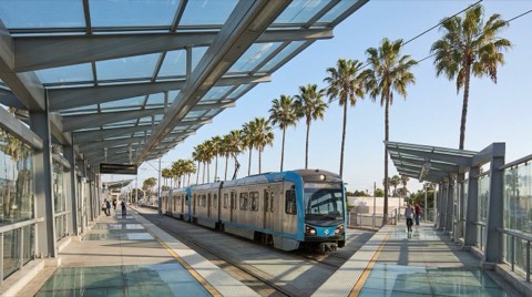 The Expo Line light rail platform in Santa Monica with palm trees along the tracks under a clear late-morning sky