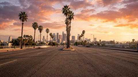 A wide Westside boulevard at golden hour stretching toward a hazy distant skyline, evoking the commute between Westwood and the rest of Los Angeles