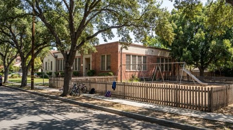A tree-shaded elementary school exterior in Los Feliz with a small playground behind a low picket fence
