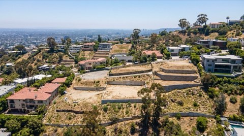 A wide daytime view of terraced Hollywood Hills lots following the natural slope of the hillside, with retaining walls and scattered homes