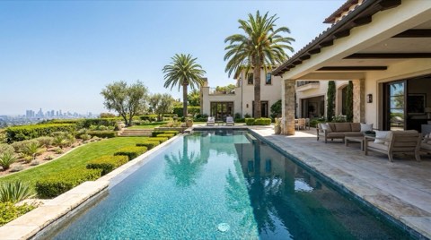 A luxury estate exterior with an infinity pool, manicured grounds, and mature palm trees