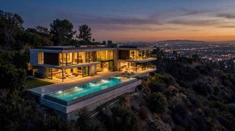 A modern glass-walled hillside estate at twilight with a glowing infinity pool overlooking a vast carpet of city lights